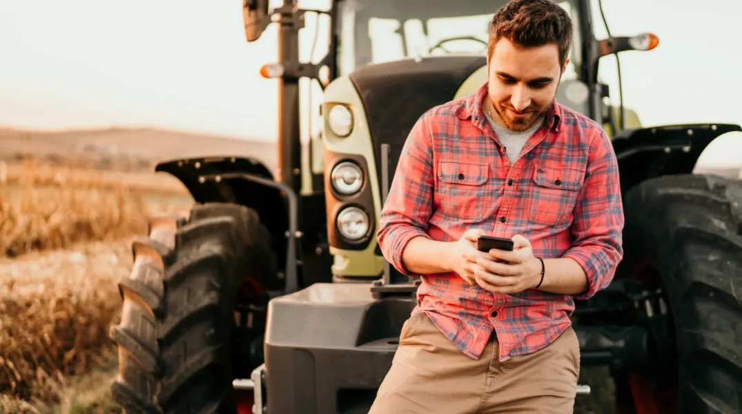 Éleveur sur son téléphone adossé à un tracteur